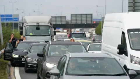 PA Media People wait by and in their vehicles on the M25