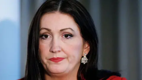 EPA/Shutterstock Emma-Little Pengelly has long black hair and bright red lipstick. She is also wearing earrings with diamonds in them and has a neutral expression.