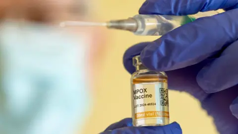 Getty Images A syringe, and a bottle of MPOX vaccine held by someone wearing clinical blue gloves