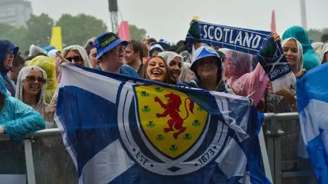 Getty Images festival fans by a barrier hold scotland flags and scarves