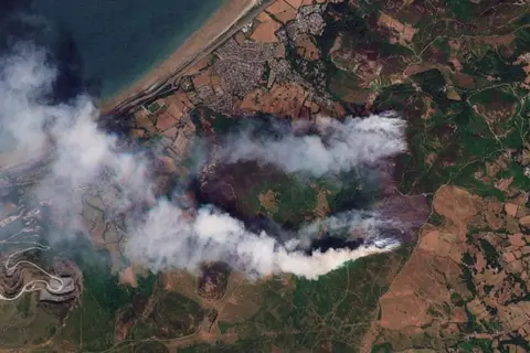 Planet Labs PBC A satellite image on Sunday of smoke rising and scorch marks on the hillsides behind Capelulo village