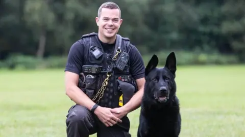 Nottinghamshire Police PC Chris Duffy kneels next to a police dog