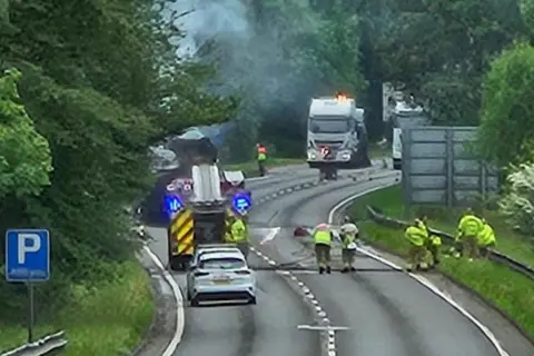 Firefighters on a section of closed dual carriageway. A fire engine and badly-burned lorry are to the left