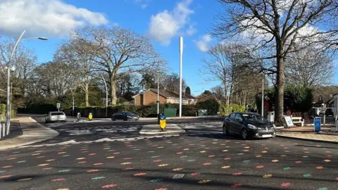 Cars driving across one of the rainbow leaf roundabouts.