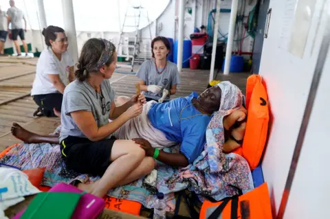 Reuters NGO Proactiva Open Arms members sit with Josepha from Cameroon onboard of NGO Proactiva Open Arms rescue boat in central Mediterranean Sea