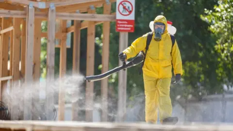 Russian Emergencies Ministry via Reuters A specialist wearing personal protective equipment sprays disinfectant while sanitising a railway station in Moscow