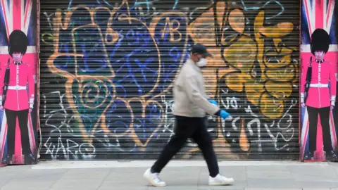 Getty Images Man wearing face mask walking past boarded shop