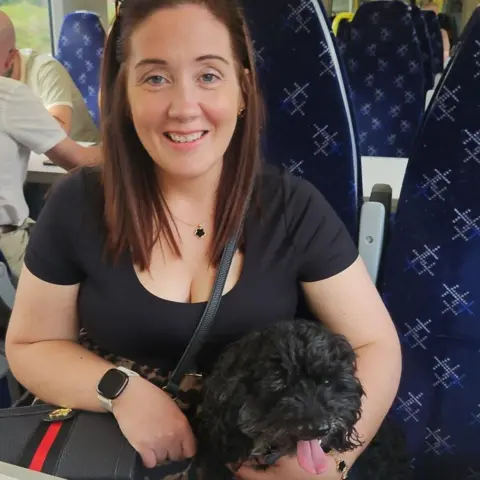 Joanne Rankin A woman with brown hair smiles while holding a black dog with its tongue sticking out.