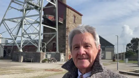 Man with grey coat standing in front of old mining engine house at Heartlands in Pool