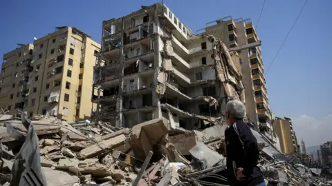 Reuters A man stands next to a damaged building in the aftermath of Israeli strikes, amid an escalation between Hezbollah and Israel, amid the U.S.-Israeli conflict with Iran, in Beirut's southern suburbs, Lebanon, March 12, 2026.