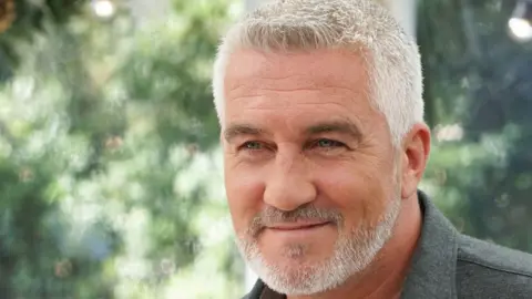 A man with silver hair and stubble smiles