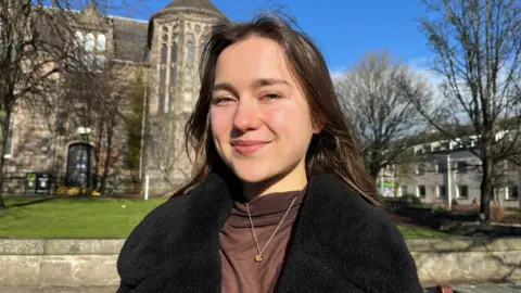 Alisa standing in the centre of the shot looking at the camera with university of Aberdeen building on the background.