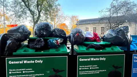 Two general waste bins with 10 full bin bags on top, as the bins are full. 