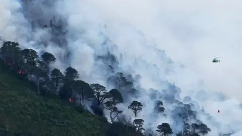 A vivid scene from the Cairngorms wildfire, with a helicopter flying over the fire
