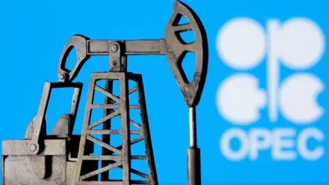 A 3D printed oil pump jack is seen in front of displayed Opec logo in white lettering on a blue background.
