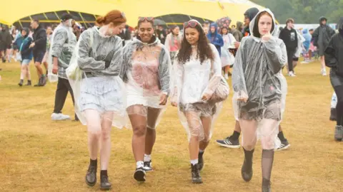 Getty Images Four women walk through the Reading crowd wearing rainproof outer clothing.