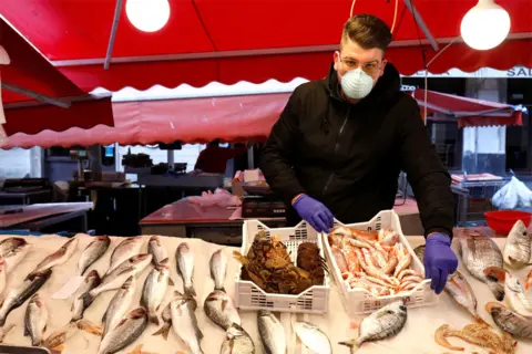 Reuters A man wearing a face mask next to a fish market stall