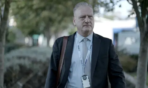 BBC/Brinkworth Productions Detective Superintendent Carl Foster looks on as he walks outside with suit and tie