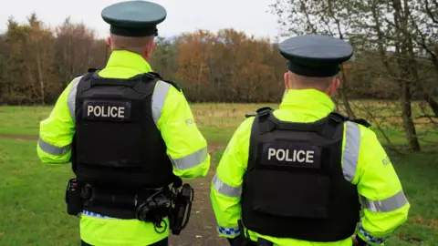 Two PSNI officer standing side by side wearing black vests and bright yellow jackets
