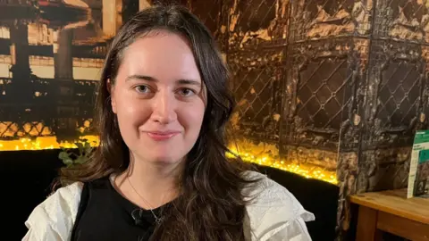 Katharine McCallum is sitting in a restaurant during a Let's Talk About Loss meet-up. She is smiling at the camera.
