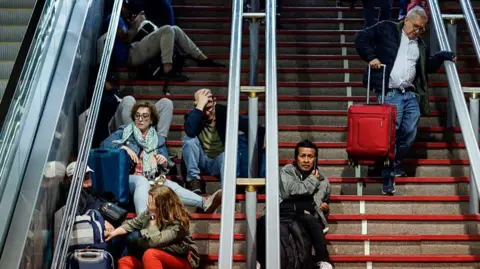 AFP via Getty Images Passengers looking stressed while sitting on the steps of Atocha train station during April's power cut.
