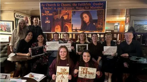 Women, men and children holding placards supporting Rachel Duffy. There is a large banner in the background.
