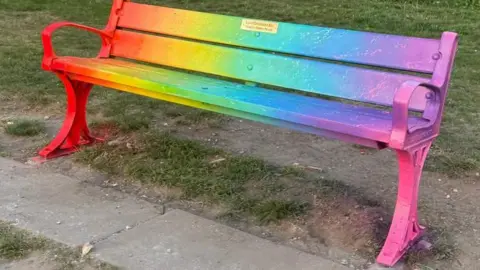 A park bench painted in different colours including yellow, pink and orange.