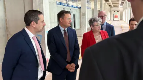 New National Biosecurity Centre in Harlow aims to fight pandemics 4 Ben Schofield/BBC Wes Streeting and a group of people in formal attire are standing in an unfinished building, with concrete wall in the background and visible construction materials