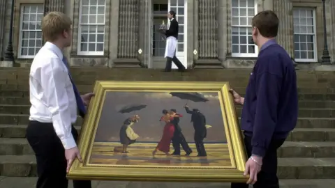 PA Media Two men carry Jack Vettriano's The Singing Butler outside Hopetoun House, where it was being auctioned in 2004. At the top of steps in the background a butler is carrying a tray with glasses and a bottle.