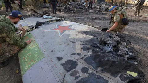 Reuters Ukrainian service members inspect parts of a Russian aerial vehicle, which local authorities assume to be a newest heavy unmanned aerial vehicle S-70 Okhotnik (Hunter) or variation of Sukhoi fighting jet, is seen in residential area of the town of Kostintynivka