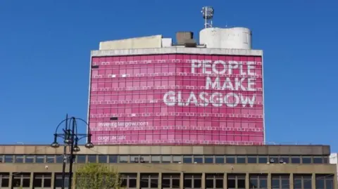 BBC A big tower, with a large pink graphic saying PEOPLE MAKE GLASGOW over the top.