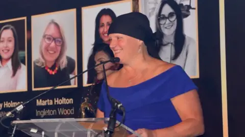 WIC/Louisa Rechenback A woman in a blue dress and black headscarf stands on an awards podium.
