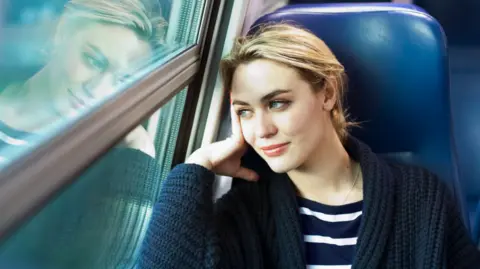 Blonde woman sitting on a train looking out the window