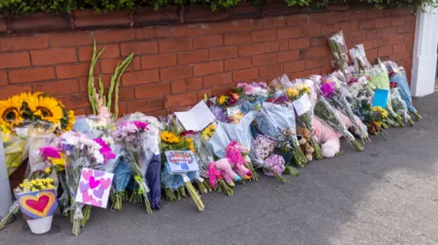 James Speakman/PA Wire Floral tributes lined up against a brick wall near the scene in Hart Street, Southport