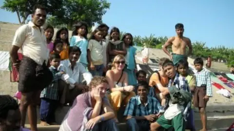 Lowri Denman Lowri sitting on steps with a large group of locals in India