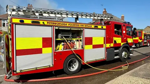 A red and white fire engine parked on a street. A red-brick residential house is behind it. 