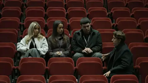 Four teenagers talking in the seats of a lecture theatre