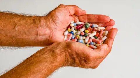 Getty Images A man holding two handfuls of pills