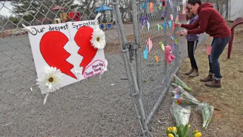 Getty Images : A woman and her daughter place a heart on a fence at a growing memorial in front of the Debert School April 20, 2020