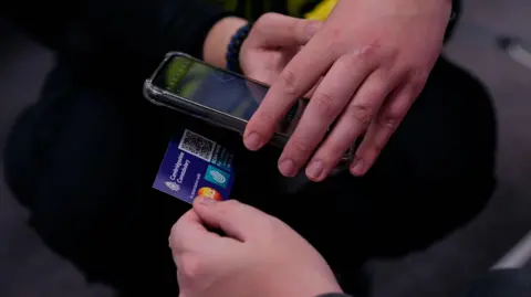 Cambridgeshire Police Image shows close-up of someone holding the card and someone else holding their phone to scan the QR code on the back of the card.
