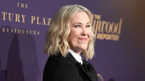 Getty Images A woman with shoulder-length blonde hair is pictured in front of a purple backdrop. She wears a black suit jacket and a white shirt.