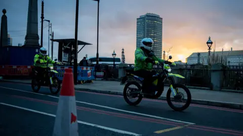 PA Media Two e-bikes clad in yellow with Police riding them. Both officers are in white helmets on a saddle. Behind them, the sun is rising