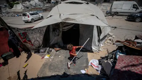 A young girl sweeps up with a brush outside a tent in Gaza City, northern Gaza (24 August 2026)