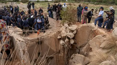 Reuters Uma multidão perto da entrada de uma mina. Cordas e uma polia podem ser vistas no topo.