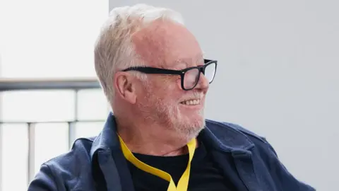 Patch Dolan Head and shoulders of Les Dennis wearing black glasses in the rehearsal room for Twelfth Night