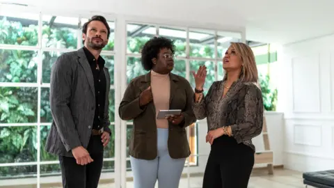 Getty Images A couple stand in the living room of a property they are viewing with an estate agent who is talking enthusiastically