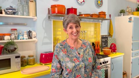 Karen Jankel, the daughter of Paddington Bear author Michael Bond, wearing a floral top and smiling at the camera, in a replica kitchen to the one featured in the Paddington Bear films