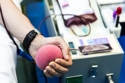 A blood donor gives blood in a medical clinic. The picture is a closeup of their hand as they squeeze a foam ball.