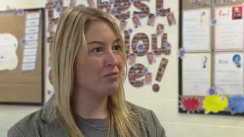 Stephanie Tempest-Mitchell, head teacher at Greengates Academy, stands in a school corridor with pupils' art in the background.