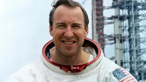 La NASA Jim Lovell sonríe mientras se para frente a una plataforma de lanzamiento vestida con su traje espacial mientras entraba para la misión Apollo 13